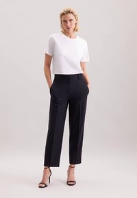 Wit topje met korte mouwen gecombineerd met zwarte, op maat gesneden broek met een klassieke pasvorm en een gladde textuur. Open schoenen met een zwarte hak maken de look compleet.