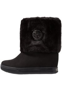 Botín negro de invierno con puño de pelo sintético y emblema redondo de logo en el lateral, suela plana de goma y material exterior suave.