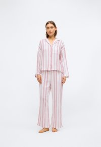 Dwuczęściowy zestaw domowy w paski wykonany z lekkiego materiału. Górna część ma zapinanie na guziki i kołnierzyk, a spodnie o luźnym kroju zdobione są pionowymi paskami.