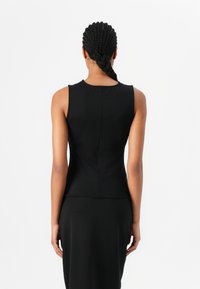 Top senza maniche nero realizzato in tessuto elasticizzato, caratterizzato da un design aderente e un dettaglio di cucitura sul retro. Il tessuto ha una consistenza liscia.