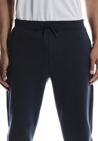 Marineblaue Jogginghose mit glatter Textur, elastischem Bund und verstellbarem Kordelzug. Verfügt über Seitentaschen und verjüngte Beine.