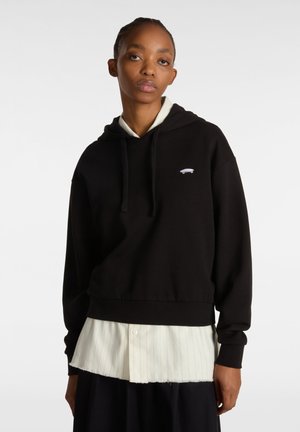 Black cropped hoodie with a drawstring hood, featuring a small gray skateboard graphic on the chest, layered over a textured cream shirt.