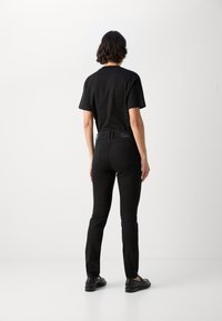 Zwarte katoenen t-shirt en taps toelopende zwarte jeans, met een minimalistisch ontwerp. De outfit heeft een gladde textuur en wordt gecombineerd met zwarte schoenen.