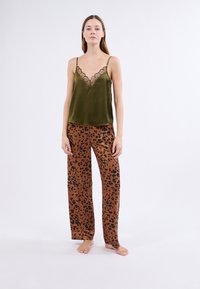Camiseta de satén verde oliva con encaje, combinada con pantalones anchos marrones que presentan un estampado de leopardo negro.