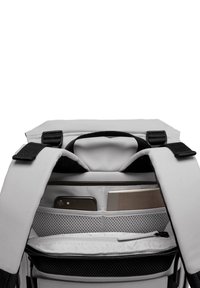 Intérieur d'un sac à dos gris avec des poches en maille, un compartiment zippé et des sections d'organisation pour un téléphone et un carnet. Les sangles noires offrent un contraste.