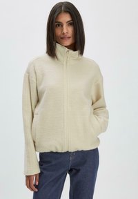 Cremfarbene Fleecejacke mit hohem Kragen, Frontreißverschluss und Seitentaschen. Lockere Passform mit langen Ärmeln, strukturiertem Stoff und ohne sichtbare Muster.