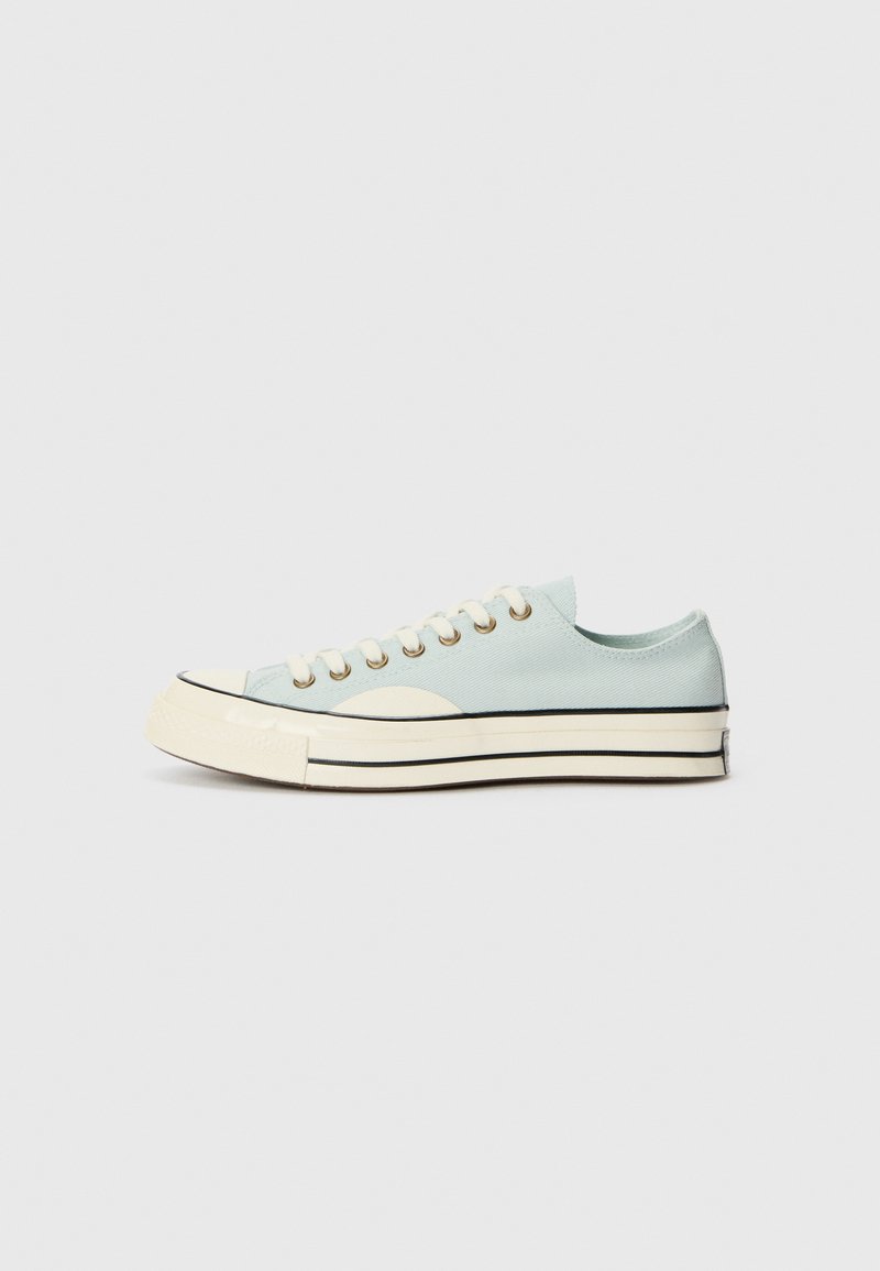 Light blue canvas sneaker with a rounded toe, white rubber sole, and black stripes. Features gold eyelets and flat laces.