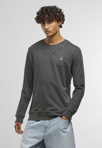 Felpa grigia scura in misto cotone, con collo tondo, maniche lunghe e un piccolo logo bianco a forma di ancora sul petto. Vestibilità casual.