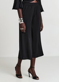 Pantaloni culotte neri realizzati in tessuto morbido e liscio con cintura elasticizzata, caratterizzati da una vestibilità ampia che cade sotto il ginocchio, abbinati a tacchi neri.