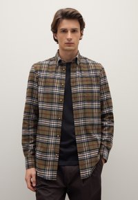 Braun-grünes kariertes Hemd mit Button-Down-Kragen, verziert mit weißen und roten Linien, getragen über einem schwarzen Hemd. Strukturierter Stoff, lässiges Design.