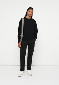 Maglione nero a maglia, pantaloni cargo neri, borsa a tracolla grigia e sneakers bianche con dettagli grigi. Design semplice, vestibilità casual, senza motivi visibili.