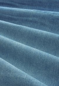 Tissu en denim bleu clair avec une texture lisse, présentant des lignes de sergé diagonales prononcées et des variations de couleur subtiles.