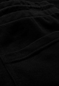 Gros plan sur un tissu noir montrant une poche cousue et une ceinture élastique froncée sur un vêtement textile doux.