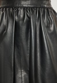 Musta nahkahame, jossa on pleatattu muotoilu, sileä pinta ja kootut vyötärö, esittelee tyylikkään ja elegantin siluetin.
