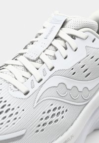 Baskets blanches de sport avec une tige en mesh texturé, des accents réfléchissants et un logo distinctif sur le côté. Les lacets sont soigneusement disposés.