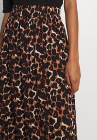 En närbild av en persons hand som vilar på en kjol med ett svart och brunt leopardmönster, som visar tyget och midjedetaljer.