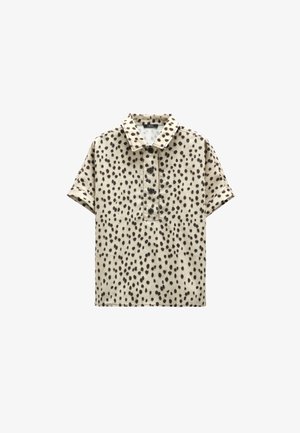 Beżowa koszula z krótkim rękawem w czarne nieregularne kropki, z kołnierzykiem i czterema czarnymi guzikami na środku przodu.