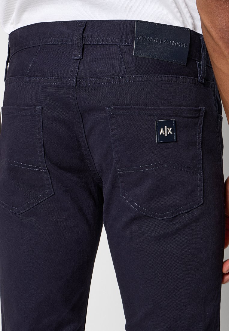 Zbliżenie na tył granatowych spodni Armani Exchange z dwiema kieszeniami, naszywką z logo na prawej kieszeni oraz skórzaną etykietą z logo na pasku.