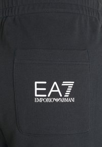 Černé bavlněné tepláky s obdélníkovou zadní kapsou se znakem EA7 Emporio Armani v bílé barvě. Měkká textura a viditelný elastický pas.