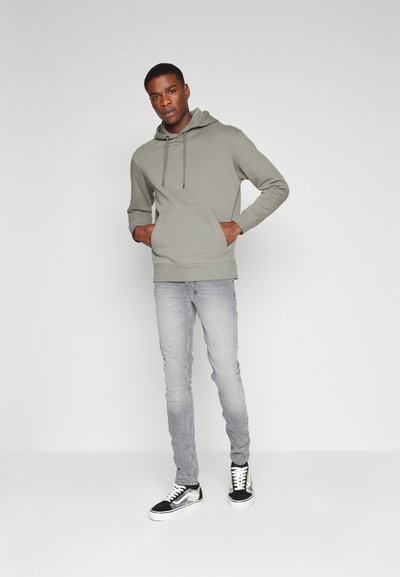 Gray cotton hoodie with drawstrings and front pocket, paired with light gray slim-fit jeans and black sneakers with white soles.