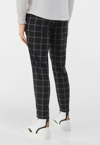 Černé kostkované kalhoty s bílými čtvercovými liniemi, vyrobené z hladké látky. Kombinovány s bílými teniskami s černými a hnědými akcenty.