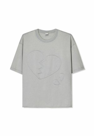 T-shirt gris à manches courtes avec un grand design de cœur brisé et de petits détails en forme de cœur, avec un col rond et une texture de tissu douce.