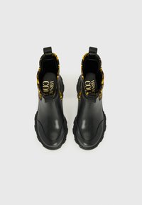 Black rubber ankle boots with a textured surface, yellow patterned collar, and prominently branded interior. Features pull tabs for easy wear.