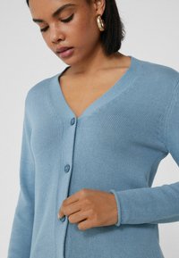 Cardigan azul claro de tejido de punto, con escote en V, dos botones y puños acanalados, de textura suave.