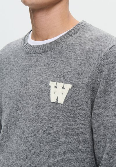 Grå strikket trøje med ribbet hals, prydet med et hvidt tekstureret "W" logo på venstre brystområde. Blødt materiale med subtil tekstur.