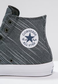 Zapatilla alta de patrón blanco y negro con suela de goma, ojales para cordones y parche de logo circular con una estrella.