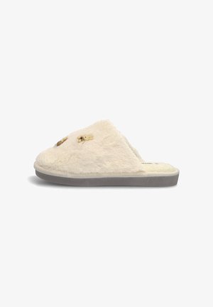 Zapatilla blanca forrada de pelo con textura suave, que cuenta con una plantilla acolchada y una suela de goma gris claro. Dos pequeños detalles de animales en la parte superior.