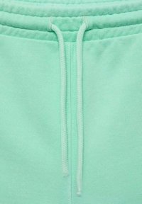 Mátově zelené tepláky s hladkým povrchem, se šňůrkou v pase a žebrovanými detaily na pase.