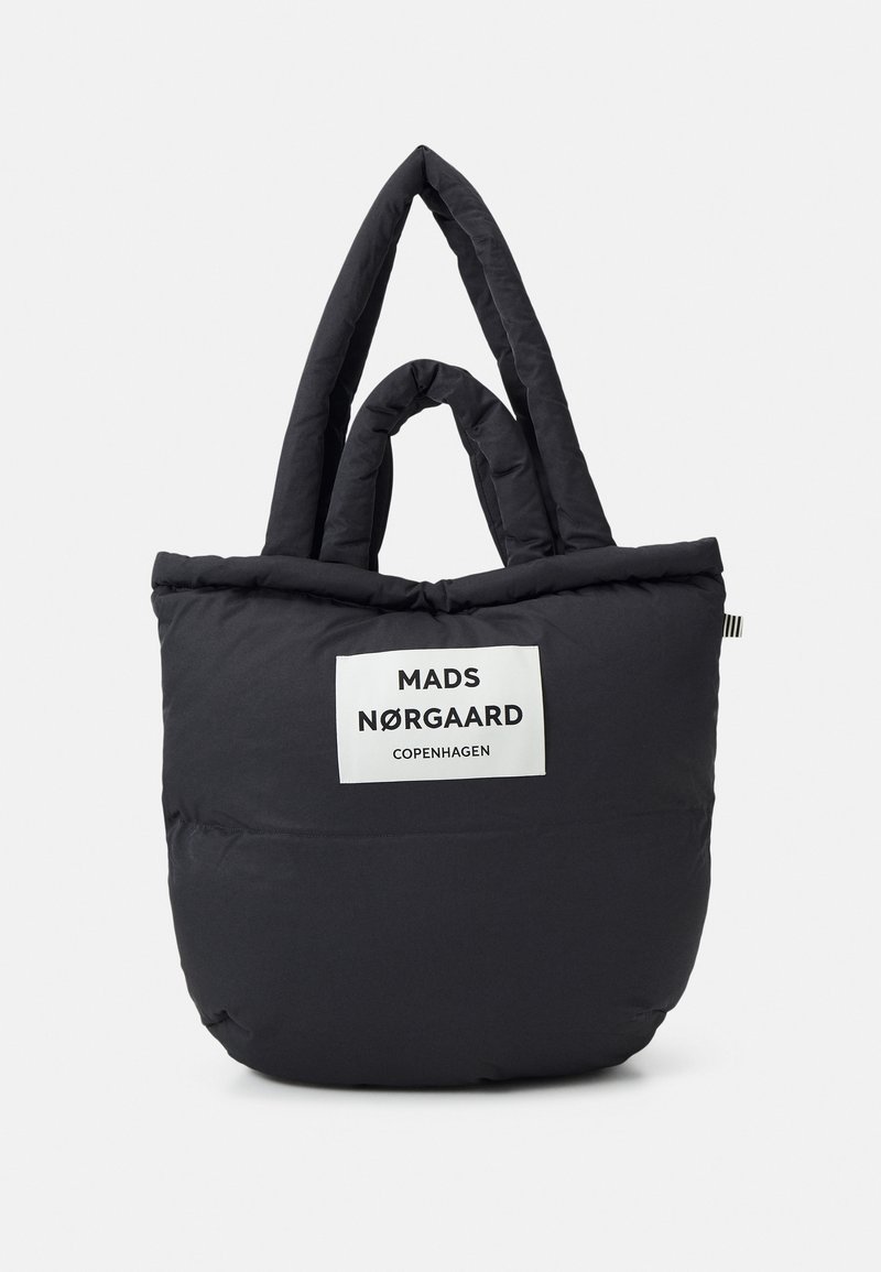 Zwarte, fluffy totebag met dubbele handvatten, voorzien van een wit label met de tekst "MADS NØRGAARD COPENHAGEN." Zachte textuur en ronde vorm.