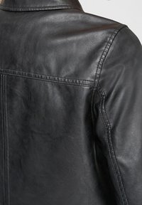 Chaqueta de cuero negra que muestra una textura suave, diseño de paneles en la parte posterior y costuras distintivas a lo largo de los hombros y las costuras.
