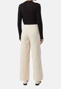 Czarna bluzka z długim rękawem połączona z kremowymi spodniami o szerokich nogawkach. Spodnie mają gładką fakturę i wysoki stan. Całość dopełniają czarne buty.