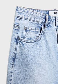 Jean en denim bleu clair effet délavé à l’acide, avec passants de ceinture, poche avant et petite poche à monnaie visible sur le côté droit.