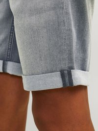Shorts en denim gris clair avec un ourlet roulé. Présentent une texture lisse et des coutures contrastées. Conçus avec une coupe décontractée et une longueur jusqu'aux genoux.