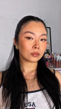 Porträt einer Person mit langen schwarzen Haaren, die goldene Creolen und geschichtete goldene Halsketten trägt, mit einem natürlichen Make-up-Look und glänzenden Lippen.