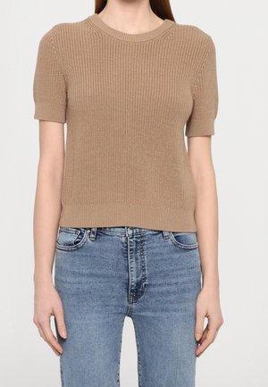 Kortærmet strikket trøje i beige med ribbet texture, rund halsudskæring og tætsiddende silhuet, parret med lyseblå jeans.
