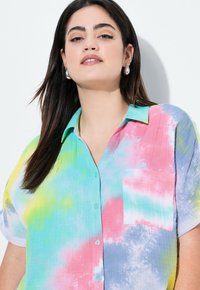 Camicia a maniche corte con bottoni in un motivo tie-dye dai colori pastello: rosa, blu, verde e giallo. Presenta una tasca sul petto e un colletto.