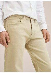 Vaaleanbeige puuvillahousut, joissa on slim fit -malli. Housuissa on etutaskut ja vetoketjukiinnitys. Kangas näyttää sileältä ja hieman teksturoidulta.