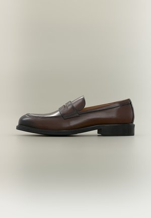 Chaussure classique penny loafer en cuir marron foncé avec semelle noire et petit talon, vue de côté sur un fond clair uni.