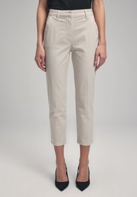 Pantalons beiges ajustés avec une coupe slim, longueur cropped, poches latérales et une texture lisse, associés à des chaussures à talons hauts noires.
