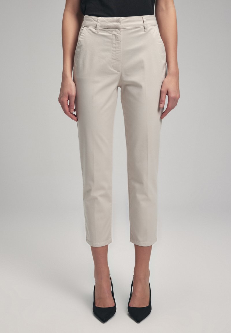 Pantalons beiges ajustés avec une coupe slim, longueur cropped, poches latérales et une texture lisse, associés à des chaussures à talons hauts noires.
