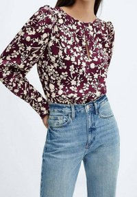 Haut à manches longues bordeaux à motifs floraux avec un détail d'encolure en trou de serrure, associé à un jean bleu clair taille haute. Le tissu présente une texture à motifs.