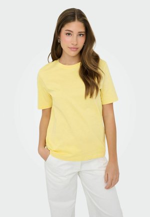 Light yellow cotton t-shirt with a round neckline and short sleeves, paired with white trousers. Smooth texture and casual fit.