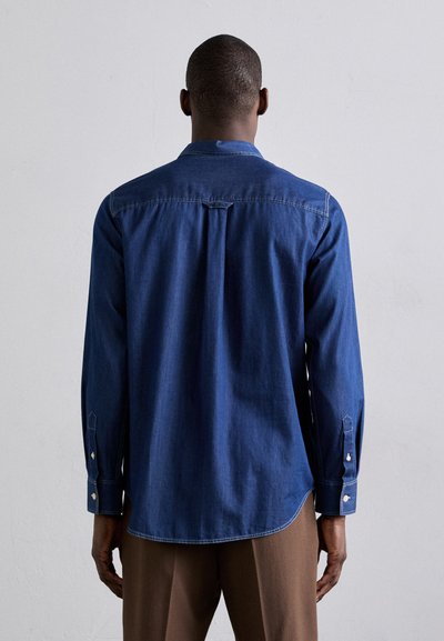 Camicia di jeans blu scuro, con maniche lunghe, collo a camicia e orlo arrotondato. Cuciture e dettagli dei bottoni visibili sui polsini.
