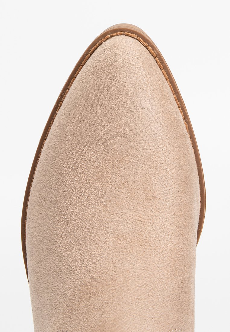 Bota marrón claro de ante hasta el tobillo con punta afilada y suela cosida en tono marrón. Textura suave con diseño minimalista y sin elementos metálicos o acentos visibles.