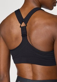 Black sports bra featuring wide adjustable straps, a hook detail at the back, and flat seams for enhanced comfort and fit.