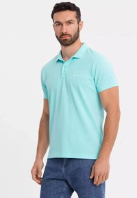 Ljusblå polo shirt i bomull med klassisk krage och treknäppt knäppning. Korta ärmar och diskret logotypdetalj på bröstet.